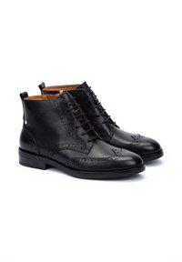 Bottes à la cheville en cuir noir avec des détails brogue, bout rond, laçage à l'avant et un talon bas. Texture lisse avec des accents métalliques subtils.