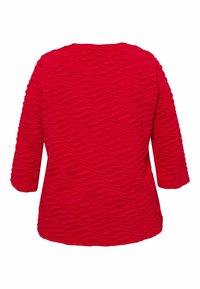 Rode top met driekwart mouwen, voorzien van een getextureerd golvend patroon over het oppervlak. Zacht, gebreid materiaal vergroot de visuele diepte.