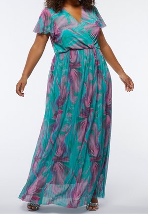 Femme portant une robe fluide turquoise avec des motifs tourbillonnants roses et violets et des manches papillon, debout les bras légèrement écartés.