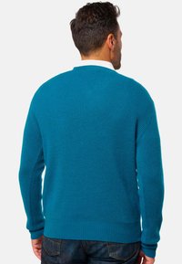 Pull en maille côtelée teal à manches longues, col rond et texture lisse, vu de dos. Associé à un jean bleu foncé.