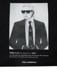 Fekete-fehér grafikus táska, amelyen egy napszemüveges férfi portréja látható, a háttérben pedig az "i-kon" és "Karl Lagerfeld" feliratok egy modern designnal.