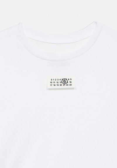 Λευκό βαμβακερό t-shirt με στρογγυλή λαιμόκοψη και ετικέτα με αριθμούς και μαύρο κύκλο, τοποθετημένη στο κέντρο κάτω από τον γιακά.