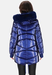 Fényes kék pufi dzseki szőrmebéléses kapucnival, halszálka mintás steppeléssel és elasztikus mandzsettákkal. Állítható húzózsinórral az alsó részen.