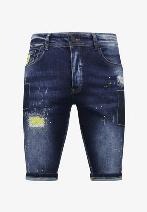 Donkerblauwe denim shorts met opgerolde pijpen, vervaagde plekken, gele verfspatten en patchdetails op de dijen.