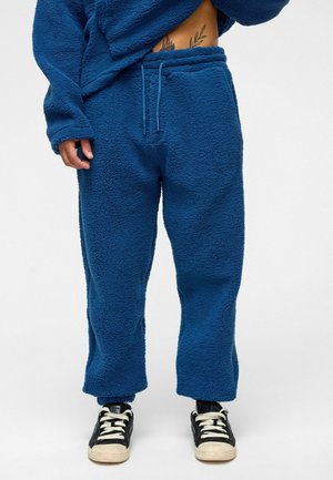 Fleece joggingbroek in diepblauw, met een elastische tailleband en een trekkoord, een losse pasvorm en een warme, gestructureerde stof; gecombineerd met zwarte sneakers.