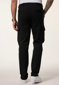 Zwarte cargobroek met een elastische tailleband, zijzakken en achterzakken. Glad materiaal met een tapse pasvorm, gecombineerd met witte sneakers.