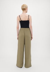 Crna bezrukavna majica u kombinaciji s labavim maslinasto zelenim hlačama s teksturiranim završetkom i elastičnom waistbands, viđena s leđa.