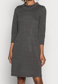 Robe en plaid gris avec un col haut et des manches trois quarts, fabriquée à partir d'un tissu texturé, présentant une silhouette ajustée et une longueur au genou.