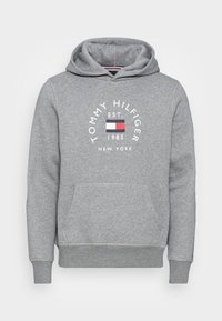 Grau Hoodie aus einem Baumwollmischgewebe. Verfügt über eine Vordertasche und eine Kapuze mit Kordelzug, mit einem Logo und Jahr in Weiß und Rot bedruckt.