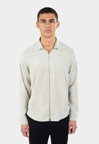 Lys grå zip-up skjorte med krave, lange ærmer, subtil tekstur og buet kantdesign. Båret sammen med sorte bukser.