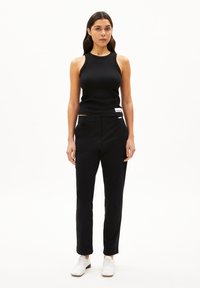 Zwarte geribbelde mouwloze top gecombineerd met op maat gemaakte zwarte broeken. Het model draagt witte schoenen. Minimalistisch ontwerp met subtiele branding op de broeken.