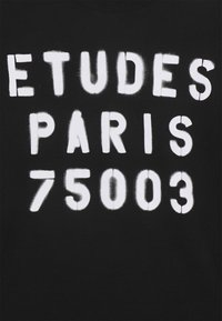 Black fabric featuring bold, white spray-painted text reading "ETUDES PARIS 75003." The letters have a slightly distressed texture.