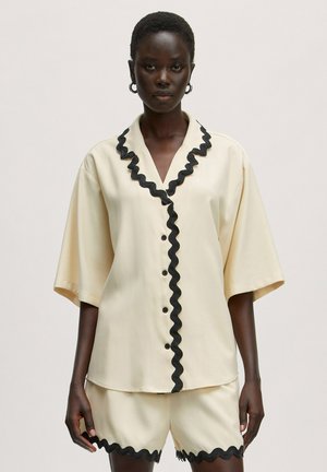 Chemise de couleur crème avec bord noir ondulé, manches courtes et boutons sur le devant ; associée à un short crème assorti avec un ourlet ondulé.
