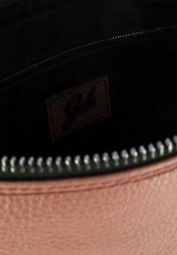 Interno di una borsa rotonda in pelle rosa con una fodera nera e cerniera. Un piccolo etichetta marrone con il nome del marchio è visibile.