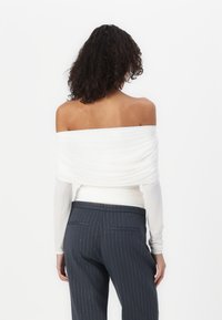 Top blanco de tirantes caídos con un diseño drapeado y mangas largas, combinado con pantalones de rayas azul oscuro. Tela suave y silueta ajustada.