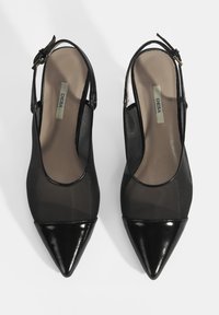 Talons aiguilles noires à bride arrière avec un bout pointu, présentant un dessus transparent et un embout en cuir verni brillant. Bride de cheville réglable pour un ajustement parfait.