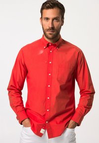 Camisa roja de manga larga con botones, hecha de algodón, que presenta un bolsillo delantero y botones blancos, combinada con pantalones blancos.