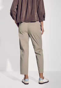Pantalons en coton beige à coupe droite avec deux poches arrière, associés à des baskets blanches et bleues, vus de l'arrière.