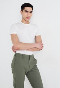 White short-sleeve t-shirt with a subtle texture paired with olive green pants featuring belt loops and a flat front.