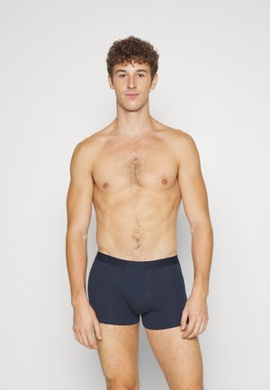 Dunkelblaue Baumwoll-Boxershorts mit einer figurschmeichelnden Passform, elastischem Bund und flachen Nähten für zusätzlichen Komfort. Das Model steht selbstbewusst vor einem schlichten Hintergrund.