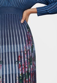 Blå randig klänning med ribbad textur, med blommönster längs nederkanten, som kombinerar vertikala och horisontella mönster.