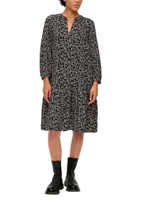 Schwarzes Blumenkleid mit langen Ärmeln, V-Ausschnitt, gerafftem Tailleneinsatz und lockerer Passform, kombiniert mit schwarzen Knöchelstiefeln. Glatte Stofftextur.