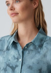 Camicia button-up blu con un motivo floreale in stile acquerello, dotata di un colletto rigido e bottoni leggeri, realizzata in un morbido tessuto testurizzato.