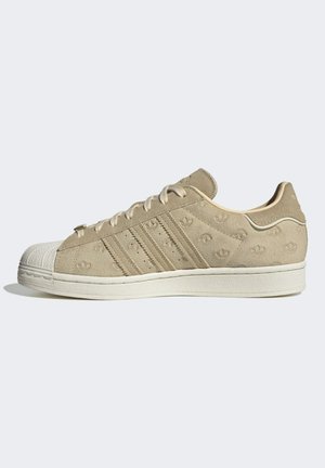 Baskets basses en daim beige avec trois bandes et logos trefoil embossés, bout et semelle en caoutchouc blanc, vues de côté.
