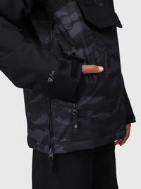 Mano con el pulgar metido en el bolsillo lateral de una chaqueta de camuflaje negro y gris oscuro, con cremallera y puño de velcro etiquetado "10K".