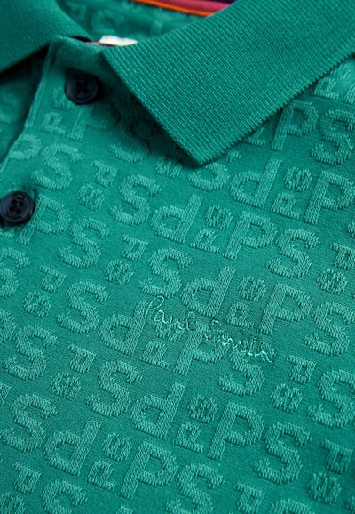 Grön polo t-shirt med texturerat mönster som har bokstäver, två svarta knappar vid kragen och en subtil broderad logotypdetalj.
