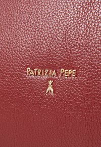 Červená texturovaná kůže se zlatým označením "PATRIZIA PEPE" a malým zlatým emblémem. Materiál má zrnitý povrch.