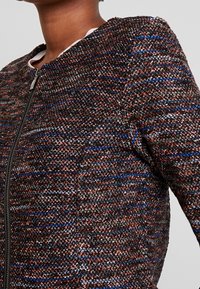 Giacca tessuta con un tessuto testurizzato nero, rosso e blu, dotata di chiusura con zip e scollo rotondo. Vestibilità sartoriale con dettagli minimi.