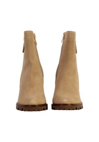 Stivaletti alla caviglia in suede beige con una silhouette slim, chiusura con zip e suola in gomma testurizzata. Presentano dettagli in ottone dorato sulla zip posteriore.