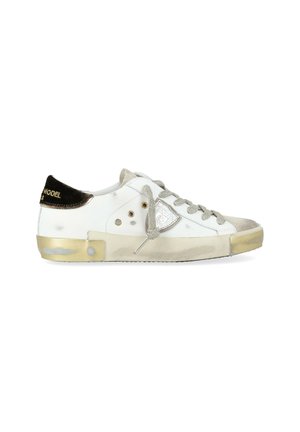 Sneaker bassa bianca con accenti beige, lacci grigi, patch metallico del logo sul lato e tab nera sul tallone con testo dorato.
