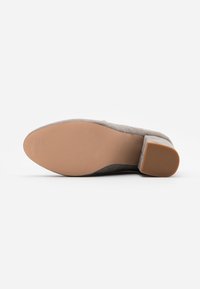 Zapato de tacón de ante gris con punta redondeada y un tacón bajo cuadrado. La suela es de goma marrón claro con líneas de agarre texturizadas.