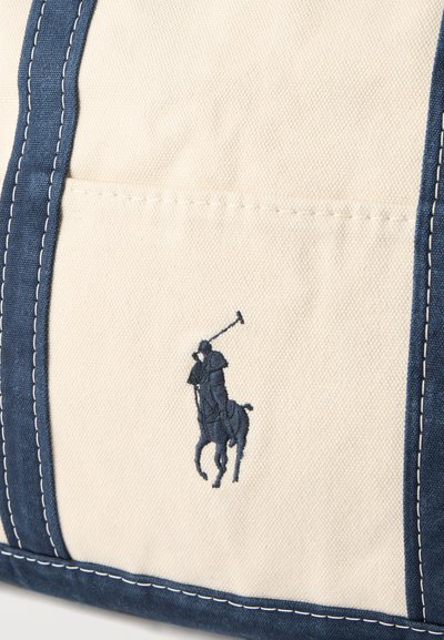 Μπεζ καμβάς με επένδυση σε ναυτικό μπλε και κεντημένο παίκτη πόλο σε άλογο, που κρατά μπαστούνι, σε ναυτικό μπλε.