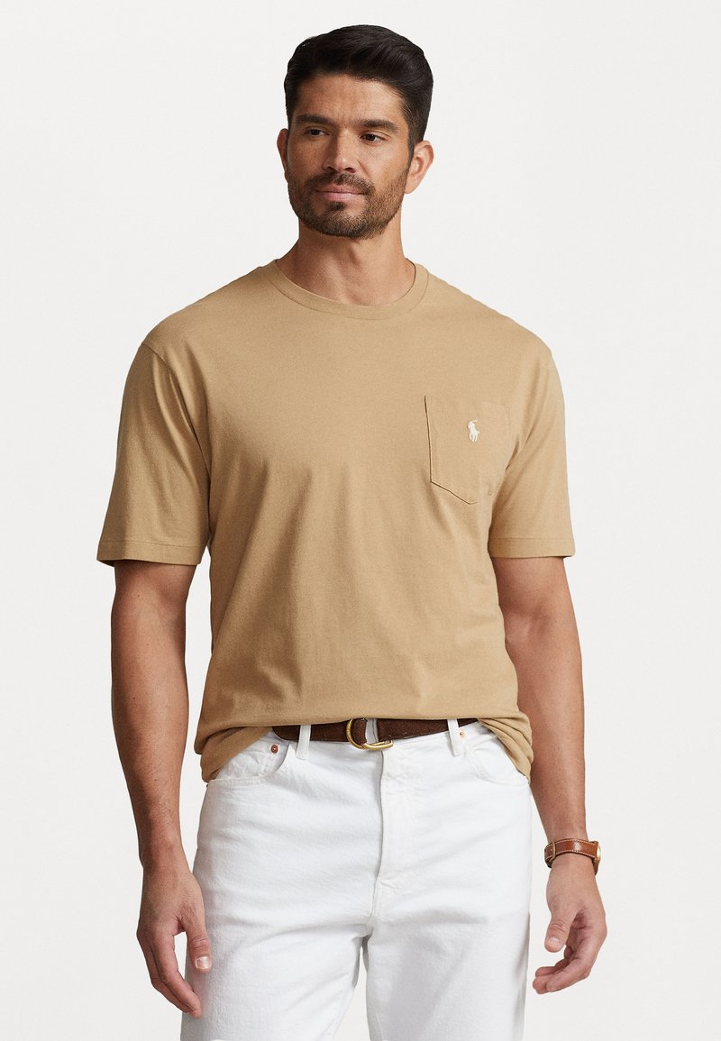 Beige bavlněné tričko s kulatým výstřihem a krátkými rukávy, s náprsní kapsou na levé straně a vyšitým logem. Nosit s bílými džíny.