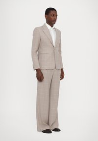 Šviesiai pilkas kostiumas su rožiniu languotu raštu. Švarkas turi struktūrizuotus pečius ir užsegimą su vienu mygtuku. Plačios kelnės užbaigia įvaizdį.