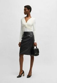 White long-sleeve top with twisted front, black leather pencil skirt, black handbag, and black high-heeled shoes with block heels.