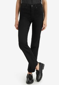 Jeans negros de pierna recta con tiro alto, que cuentan con cinco bolsillos, pasadores para cinturón y cierre de botón. Combinados con mocasines negros.