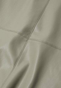 Tissu en cuir vert clair à texture lisse, présentant des coutures discrètes et un tombé doux. Met en avant des lignes de coutures intersectées.