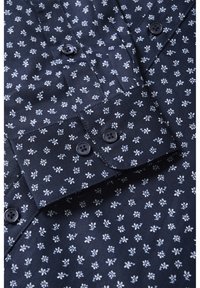 Marineblauwe shirt met een klein wit bloemenpatroon, zichtbare knoopmanchetten en knopen aan de voorkant.