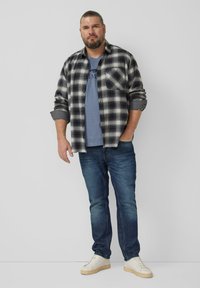 Koszula flanelowa w kratę w czarno-białe wzory, noszona na jasnoniebieskim t-shircie, zestawiona z ciemnymi dżinsami i białymi trampkami. Styl casual.