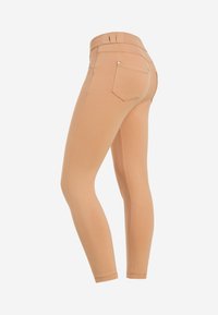 Leggings couleur chair avec une coupe slim, fabriqués en matière extensible, dotés d'une taille haute et de deux poches arrière. Texture lisse.