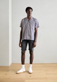 Camisa de manga corta con lunares azules sobre un fondo blanco, combinada con pantalones cortos de mezclilla grises y zapatillas blancas con suelas de color beige claro.