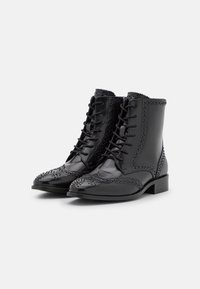 Bottines en cuir noir avec un bout arrondi, un laçage sur le devant, des perforations décoratives et des accents texturés le long des bords.