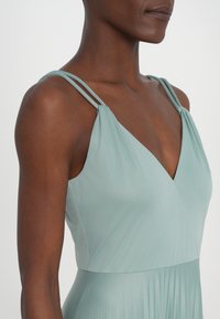 Robe vert clair avec une jupe plissée, dotée d'un décolleté en V et de fines bretelles. Texture lisse, drapé élégant.