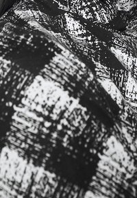 Czarnobiała tkanina wzorzysta z wyrazistym wzorem siatki, na której znajdują się teksturowane linie, kontrastujące kształty i detale liniowe.