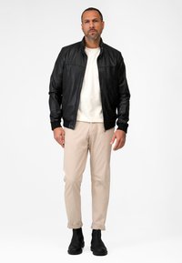 Black leather jacket with a zip closure, beige pants, and black ankle boots. The jacket features ribbed cuffs and a stand-up collar.