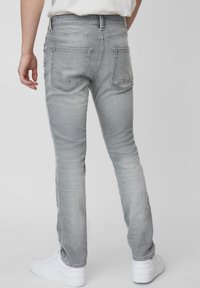 Jeans grigi chiari con una vestibilità slim, dotati di tasche posteriori, leggere sfumature e orlo pulito, abbinati a sneaker bianche.